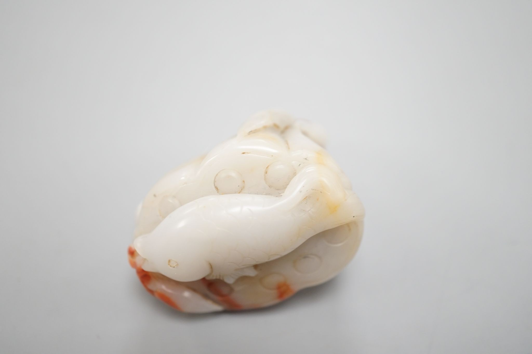 A Chinese pale celadon and russet jade 'lotus pod and fish' carving 6cm